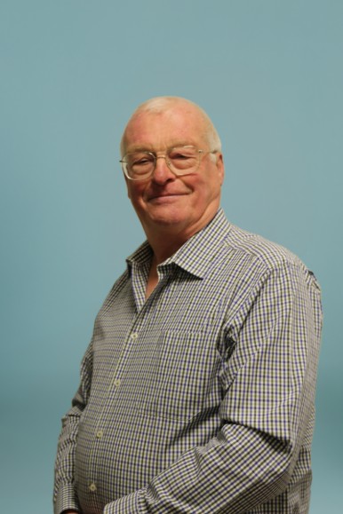 Portret van een man met bril en geruit overhemd, staand voor een effen blauwe achtergrond. (vergroot foto)