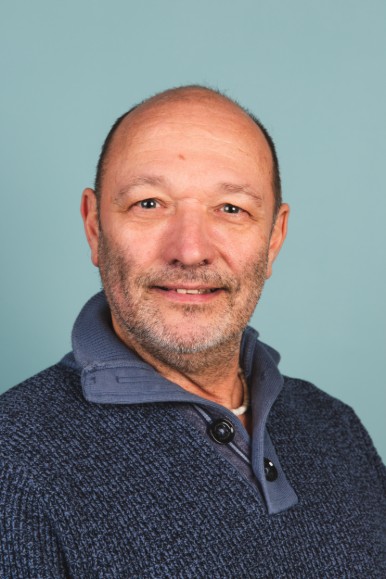 Man met kort haar, lichte baard en donkerblauwe trui tegen blauwe achtergrond (vergroot foto)