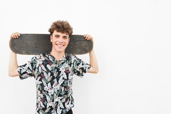 smiling-man-holding-skateboard-his-shoulder-against-white-backdrop